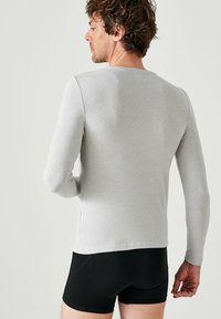 Maglietta grigia a maniche lunghe realizzata in tessuto morbido, con scollo rotondo e design aderente, abbinata a pantaloni boxer neri.