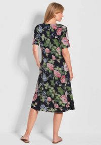 Blumenkleid in Schwarz mit kurzen Ärmeln, verziert mit rosa und blauen Blumen. Fließendes, knielanges Design in leicht A-Linien-Form ohne sichtbare Verschlüsse.