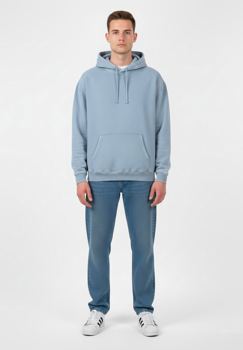 Hoodie bleu clair avec une poche frontale, des cordons de serrage et des poignets côtelés, assorti à un jean bleu moyen et des baskets blanches avec des rayures noires.