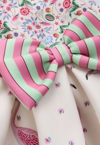 Iso kangasrusetti, jossa on vaaleanpunaisia ja vihreitä raitoja, kukka- ja flamingokuviollisen kankaan taustalla.