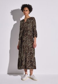 Vestido de estampado de leopardo con mangas tres cuartos y un dobladillo en capas, hecho de un tejido ligero en tonos marrón y beige, combinado con zapatillas blancas.