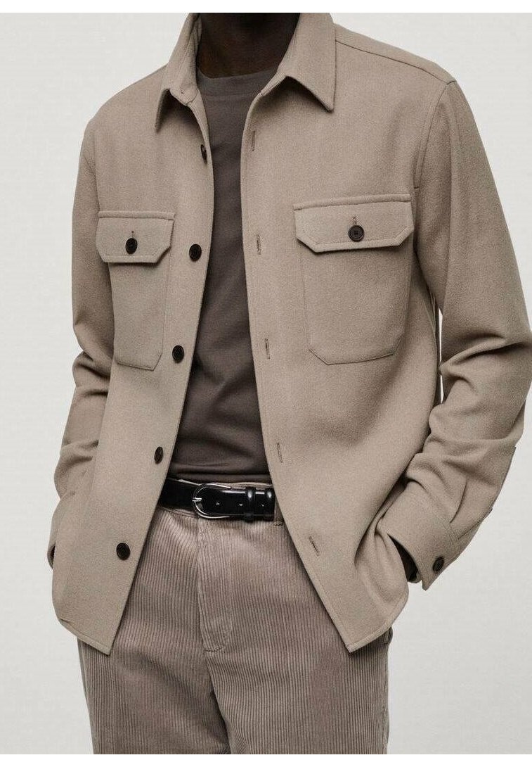 Beige wollen blazer met twee voorzakken, zwarte knopen en een puntige kraag, gecombineerd met een grijs shirt en corduroypantalon.