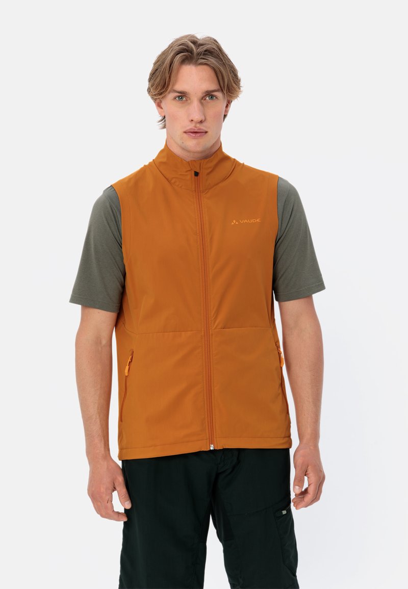 Orangeneste ärmellose Jacke mit hohem Kragen, Reißverschluss vorne und seitlichen Taschen. Getragen über einem dunkelgrünen Kurzarmhemd. Glattes, leichtes Material.