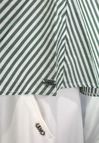 Camicetta a righe verdi e bianche con etichetta logo "SUN68" in argento, abbinata a pantaloni di stoffa bianchi con un accento logo "LUGO" in argento.