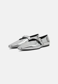 Silver metallic shoes with a pointed toe design and cut-out detailing. Features a side strap with buckle hardware. Flat black sole.