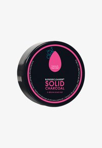 Nettoyant solide au charbon dans un emballage noir avec une étiquette accentuée de rose. Comprend un tapis de nettoyage en silicone et présente une forme arrondie et compacte.