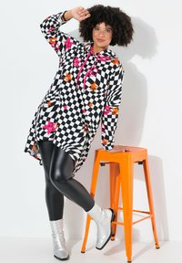 Zwart-wit geruite hoodie jurk met roze en oranje steraccenten, gecombineerd met glanzende zwarte leggings en zilveren enkellaarsjes.