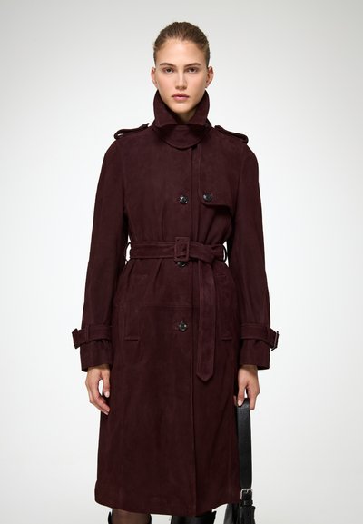 Burgundská semišová trench coat s vysokým golierom, dvojradovým zapínaním, bočnými vreckami a zodpovedajúcim pásom v p�áse. Hladká textura.