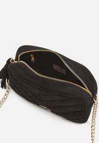 Černá svůdná kůže prošívaná crossbody kabelka se zlatým zipem, řetízkovým popruhem a detailem s třásněmi. Interiér obsahuje zipovou kapsu a textilní podšívku.