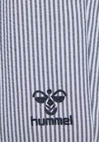 Svart och vit randig textil med en texturerad logotyp som har ett biemblem och ordet "hummel" nedanför.