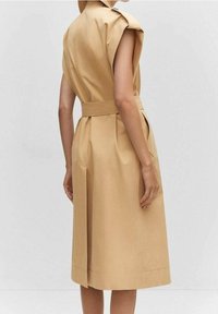 Karmelowa sukienka bez rękawów z paskiem w talii, plisowanym dołem i detalami na ramionach. Wykonana z gładkiego materiału o strukturalnym fasonie.