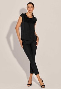 Schwarzes, ärmelloses Top mit Rundhalsausschnitt, kombiniert mit maßgeschneiderten schwarzen Hosen im slim Fit. Glatte Stoffqualität mit einem dezenten Glanz.