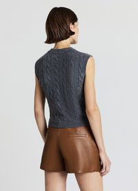 Pull sans manches en maille torsadée gris foncé avec une coupe ajustée et un ourlet côtelé. Associé à un short en cuir marron avec des poches arrière.