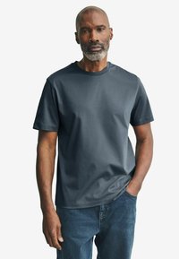 Camiseta de manga corta en gris oscuro con cuello redondo, hecha de algodón, textura suave, combinada con jeans azules, con un corte relajado.