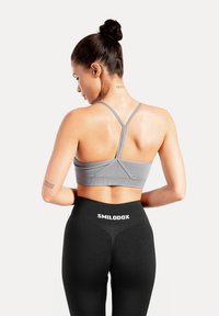 Brassière de sport grise avec fines bretelles réglables, associée à un legging noir taille haute avec un logo blanc "SMILODOX". Texture lisse.