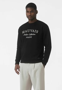 Μαύρο φούτερ με λευκό κείμενο «MAUVAIS Atelier Collection MMXVIII.» Μακριά μανίκια και στρογγυλή λαιμόκοψη με ριμπ μανσέτες και τελείωμα.
