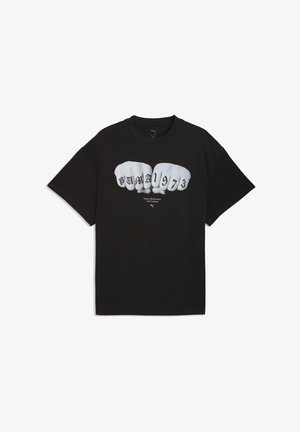 Fekete rövid ujjú póló, amelyen két ököl látható, tetoválásokkal, amelyek az ujjperceken "PUMA 1973" feliratot formáznak, alatta pedig kis méretű szöveg található.