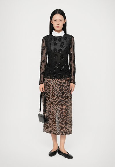 Haut transparent noir avec broderies florales en perles, superposé sur une jupe midi à imprimé léopard, accompagné de ballerines noires et d'un petit sac à main.