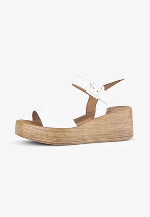 Sandalias de plataforma de cuero blanco con una amplia tira en la parte delantera y correa ajustable en el tobillo. Tacón de cuña con textura de madera, aproximadamente de cinco centímetros de altura.