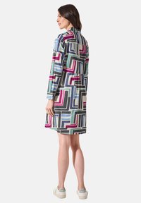 Farbenfrohes, gemustertes Kleid mit geometrischen Designs in Blau, Schwarz, Pink und Grün. Lange Ärmel und eine leicht geraffte Taille mit einem Kragen-Ausschnitt.