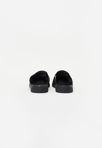 Sort slip-on sko med perforeret overdel, blød indersål og flad gummisål, der fremviser en enkel og funktionel stil.