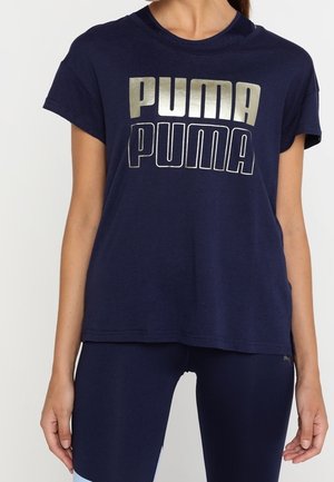 Camiseta de algodón azul marino con mangas cortas, que presenta un gran logo metálico plateado de "PUMA" impreso en el pecho. Cuello redondo.