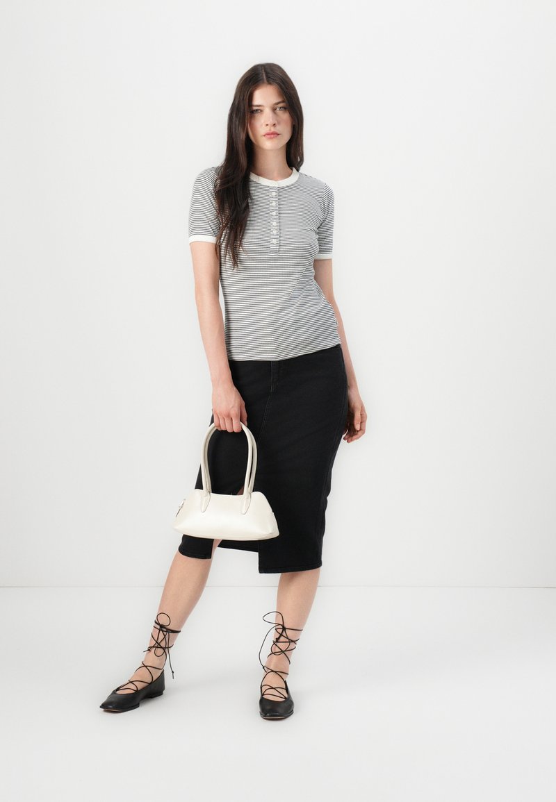 Szara pasiaste bluzka z krótkim rękawem z zapięciem na guziki, zestawiona z czarną spódnicą do kolan. Dodatki to mała biała torebka i czarne płaskie buty z sznurówkami.