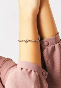 Bracciale di perle d'argento con un ciondolo a forma di cerchio che rappresenta il simbolo della pace. Il cinturino è flessibile e presenta una finitura liscia e riflettente.