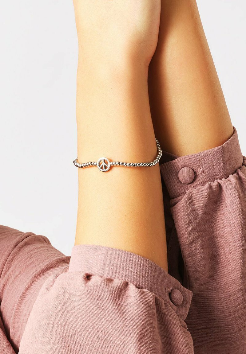 Bracciale di perle d'argento con un ciondolo a forma di cerchio che rappresenta il simbolo della pace. Il cinturino è flessibile e presenta una finitura liscia e riflettente.