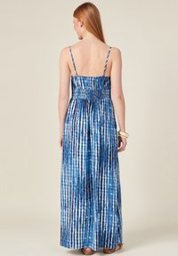 Langes blaues Kleid mit dünnen Trägern, das ein gerafftes Oberteil, vertikale Streifen und einen fließenden Saum aufweist. Der Stoff hat eine glatte, leichte Textur.