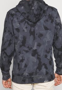 Felpa con cappuccio di colore grigio scuro con motivo camouflage. Materiale morbido, maniche lunghe e tasca a marsupio. Presenta polsini e orlo a costine.