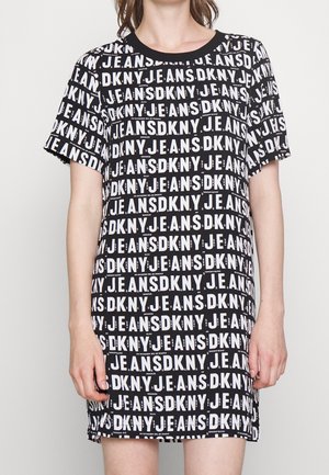 Person, die ein schwarzes kurzärmeliges Kleid mit wiederholtem weißen Textmuster mit der Aufschrift "DKNY JEANS" trägt.