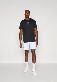 Zwart T-shirt met korte mouwen en ASICS-logo, gecombineerd met witte korte broek met een klein logo op de zoom, aangevuld met witte sportschoenen.