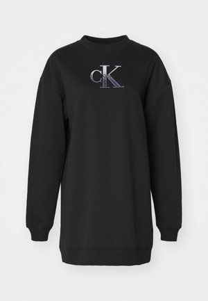 Svart genser laget av mykt stoff, med rund hals, oversized passform og "CK"-logo i grå og hvit brodering på forsiden.
