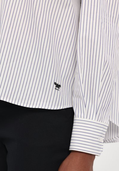 Witte shirt met blauwe verticale strepen, voorzien van een zwarte geborduurde accent aan de zoom en een manchet met knoopdetail.