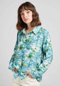 Chemise boutonnée en tissu léger avec un motif floral bleu, vert et rose, à manches longues et col. Poches sur les côtés.