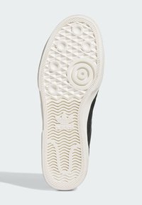 Černé tenisky s bílou texturovanou gumovou podrážkou. Obsahují kruhové úchyty a vlnící se linie, s logem viditelným poblíž paty.