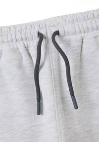 Pantalones de chándal grises claros con una cinta elástica en la cintura, que cuentan con cordones negros y puntas de plástico. La tela tiene una apariencia suave y texturizada.