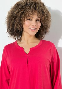 Maglia a maniche lunghe con scollo a V in un vivace rosa, realizzata in tessuto morbido con dettaglio a bottone sul collo e una vestibilità comoda.
