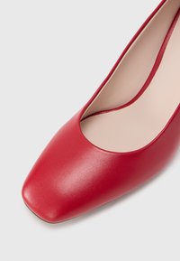 Piros bőr női cipő négyzet alakú orrával és sima textúrával, felülről, enyhén ferde szögből, fehér háttéren bemutatva.