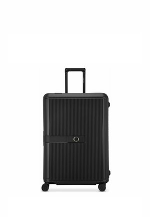 Maleta rígida negra con ranuras verticales, un asa retráctil, cuatro ruedas y una correa frontal con un cierre circular.