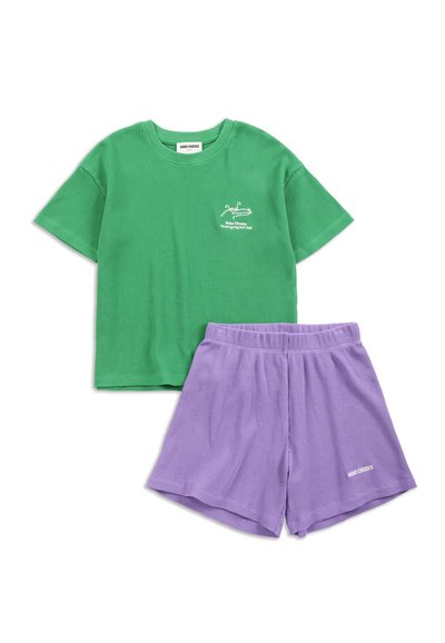 Camicia verde a maniche corte con trama, piccolo logo bianco e pantaloncini elasticizzati viola con logo su sfondo bianco.