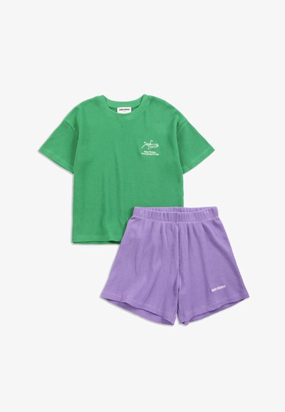 Camicia verde a maniche corte con trama, piccolo logo bianco e pantaloncini elasticizzati viola con logo su sfondo bianco.