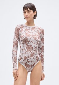 Long-sleeve swimsuit in brown with a white floral pattern, featuring a high neck and fitted design, made from smooth, stretchy material.