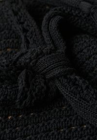 Tejido de punto negro con un patrón texturado, que presenta bucles entrelazados y una sección atada. Material detallado, suave y flexible.