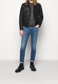 Svart läderjacka med två framfickor, grå t-shirt, ljusblå denimjeans och svarta snörstövlar med kraftig sula.