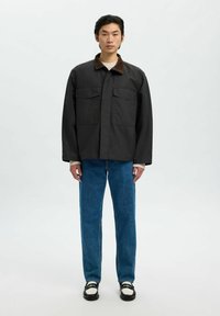 Svart jacka med en brun kordfloddsjock, två bröstfickor, parat med blå raka jeans och kontrasterande svarta och vita skor.