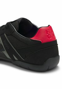 Czarny sportowy but wykonany z siateczki i materiałów syntetycznych, z teksturowaną podeszwą środkową. Jasnoczerwony akcent na pięcie z wytłoczonym logo.
