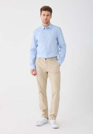 Light blue button-up shirt, beige chinos, and white sneakers. The outfit features a classic design with a smooth texture and subtle detailing.