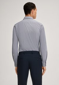 Langärmliges Hemd in Hellblau mit geometrischem Muster, ausgestattet mit einem spitzen Kragen und Knopfmanschetten, kombiniert mit dunkelblauen maßgeschneiderten Hosen.